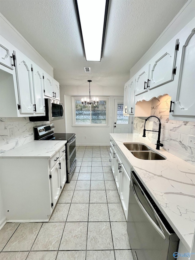 kitchen with hanging light fixtures, stainless steel appliances, backsplash, white cabinetry, and sink