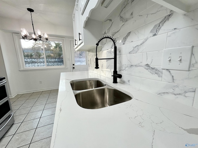 kitchen with hanging light fixtures, a notable chandelier, light stone counters, sink, and white cabinetry