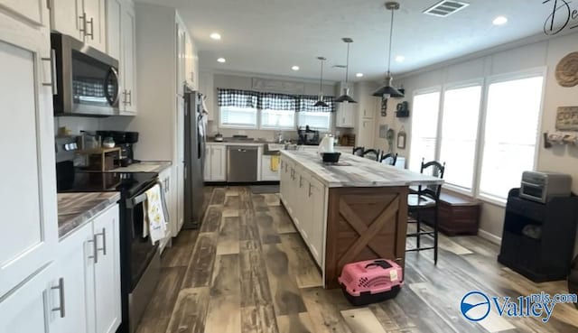 kitchen featuring white cabinetry, hanging light fixtures, dark wood-type flooring, stainless steel appliances, and a kitchen island