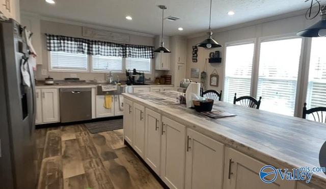 kitchen featuring white cabinets, ornamental molding, appliances with stainless steel finishes, decorative light fixtures, and dark hardwood / wood-style flooring