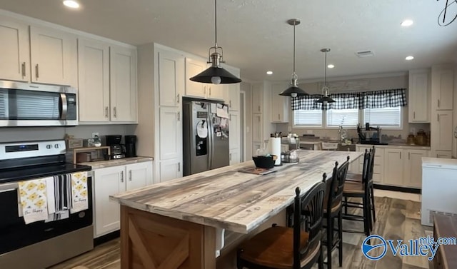 kitchen with appliances with stainless steel finishes, decorative light fixtures, a center island, white cabinetry, and a breakfast bar area