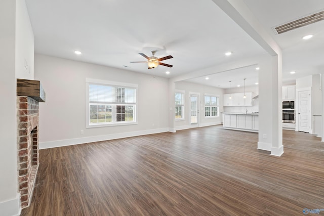 unfurnished living room featuring baseboards, visible vents, dark wood-type flooring, a brick fireplace, and recessed lighting