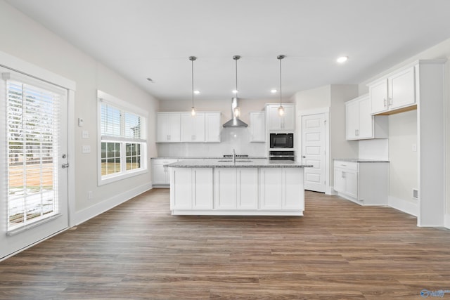 kitchen featuring black microwave, white cabinets, a center island with sink, and hanging light fixtures