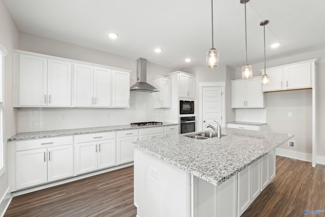 kitchen featuring white cabinets, wall chimney exhaust hood, hanging light fixtures, a kitchen island with sink, and a sink