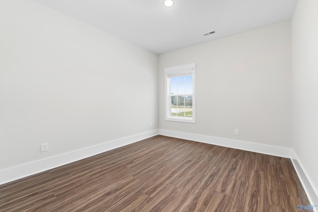 spare room featuring dark wood-style flooring, visible vents, and baseboards