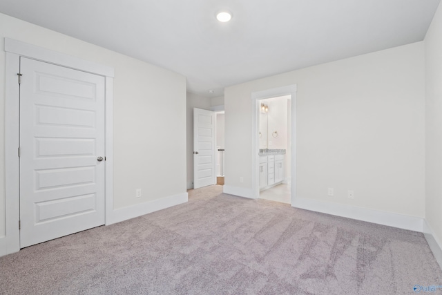 unfurnished bedroom featuring light carpet, baseboards, and ensuite bathroom