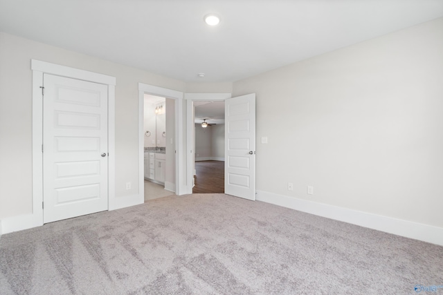 unfurnished bedroom featuring baseboards, ensuite bathroom, and light colored carpet