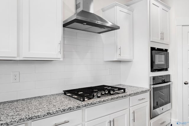 kitchen featuring wall chimney exhaust hood, appliances with stainless steel finishes, light stone counters, white cabinetry, and backsplash