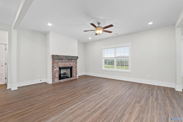 unfurnished living room with dark wood-style floors, a brick fireplace, and baseboards