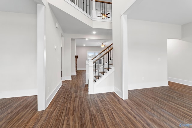 interior space featuring a towering ceiling, dark wood-type flooring, a ceiling fan, baseboards, and stairs