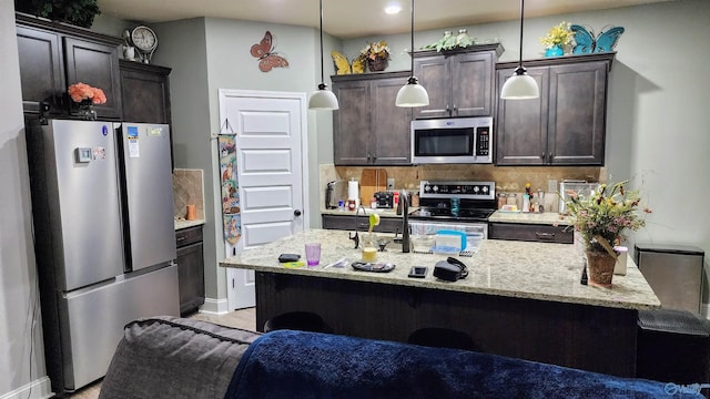 kitchen with hanging light fixtures, decorative backsplash, light stone countertops, stainless steel appliances, and dark brown cabinets