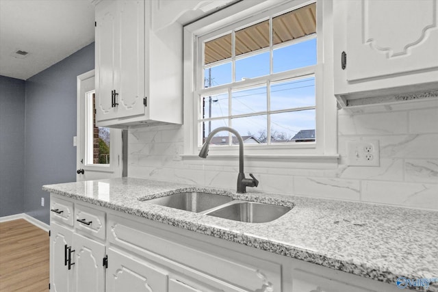 kitchen with light stone countertops, white cabinetry, sink, and tasteful backsplash