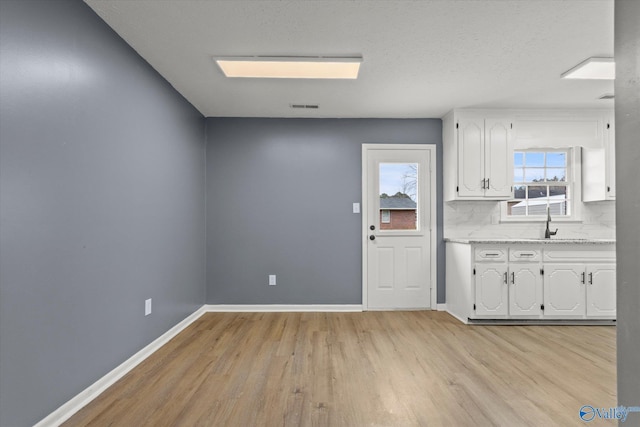 kitchen featuring white cabinets, tasteful backsplash, light hardwood / wood-style flooring, and light stone counters