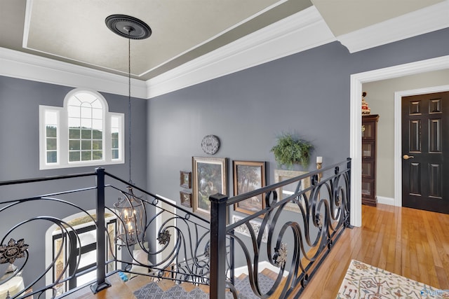 hall featuring a notable chandelier, crown molding, wood-type flooring, and a raised ceiling