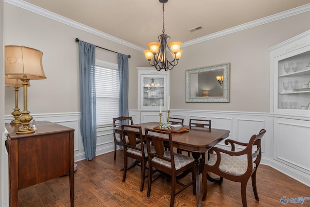 dining room featuring crown molding, a chandelier, dark wood-style floors, a decorative wall, and a wainscoted wall