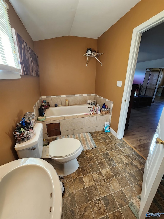 bathroom with vaulted ceiling, sink, hardwood / wood-style flooring, tiled bath, and toilet