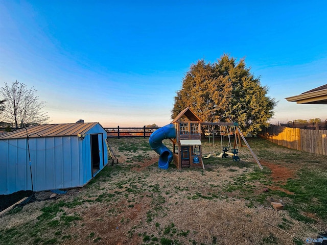 view of playground with a fenced backyard, a lawn, an outdoor structure, and a shed