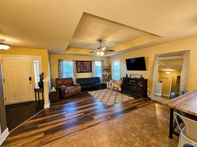 living area featuring a fireplace, a tray ceiling, wood finished floors, and a ceiling fan