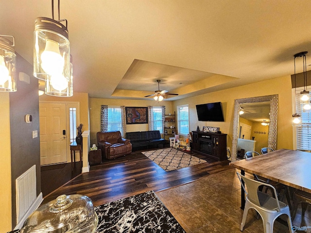 living room featuring visible vents, a fireplace, wood finished floors, a raised ceiling, and a ceiling fan