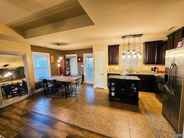 kitchen with a center island, light countertops, stainless steel refrigerator with ice dispenser, black electric range oven, and a sink