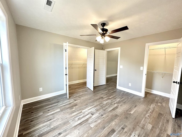 unfurnished bedroom featuring baseboards, wood finished floors, a spacious closet, a textured ceiling, and a closet