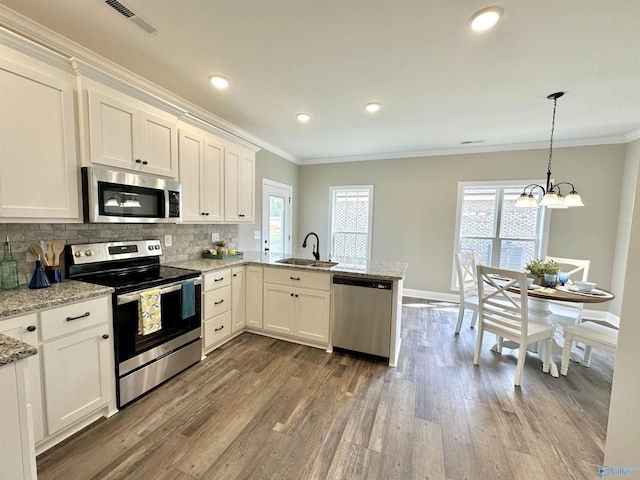 kitchen featuring visible vents, appliances with stainless steel finishes, a peninsula, crown molding, and a sink