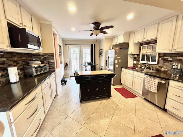 kitchen with light tile patterned floors, crown molding, ceiling fan, backsplash, and stainless steel appliances