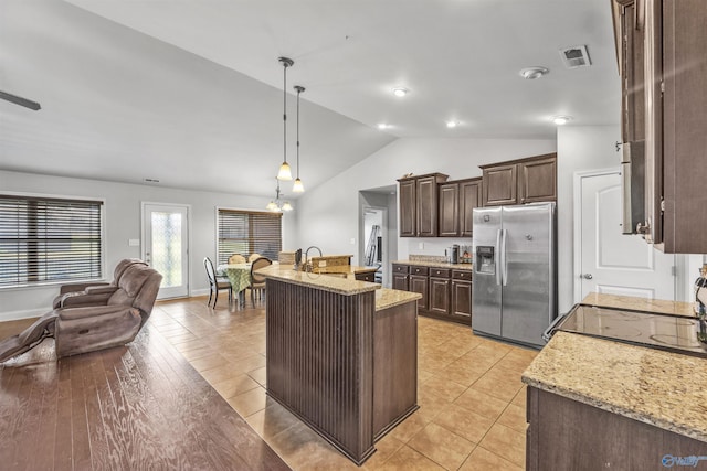 kitchen with hanging light fixtures, stainless steel fridge, light stone countertops, and an island with sink