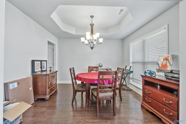 dining area featuring dark wood-type flooring, a notable chandelier, and a tray ceiling