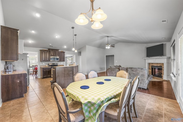 tiled dining area with ceiling fan with notable chandelier, a fireplace, and vaulted ceiling