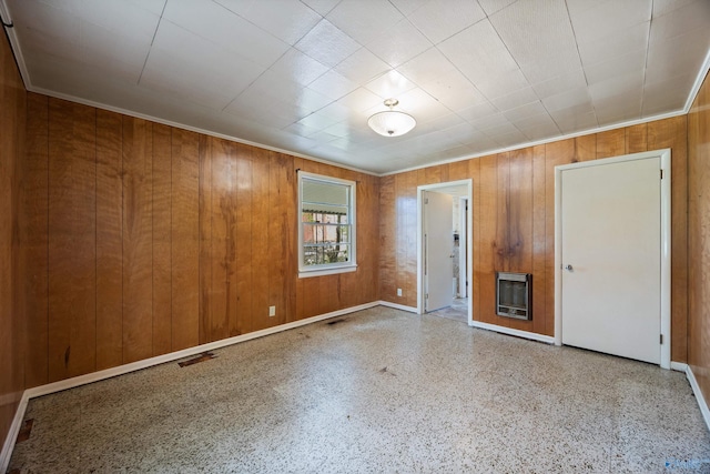 spare room featuring wood walls, baseboards, heating unit, visible vents, and ornamental molding