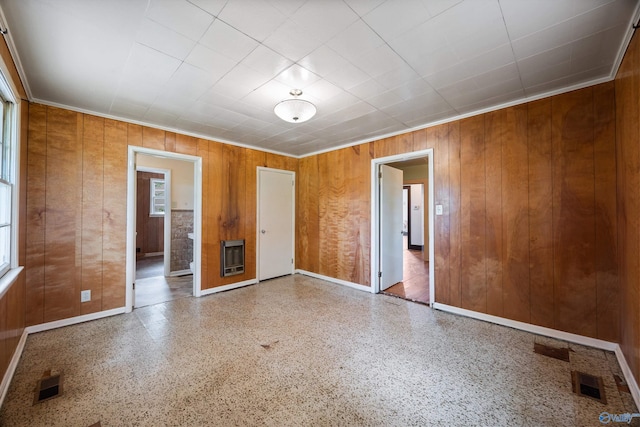 empty room featuring heating unit, baseboards, wooden walls, and visible vents