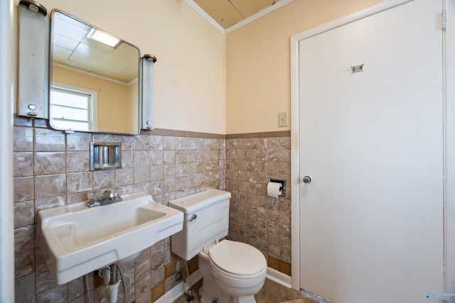half bath with toilet, tile walls, ornamental molding, and a sink