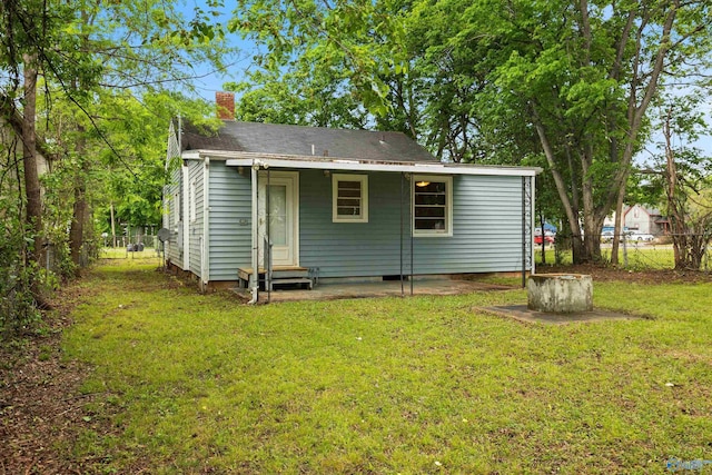 back of property with entry steps, fence, a chimney, and a lawn