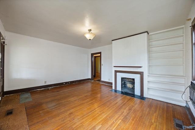 unfurnished living room featuring visible vents, baseboards, built in shelves, hardwood / wood-style flooring, and a fireplace with flush hearth