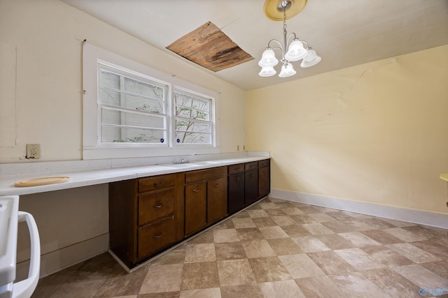 kitchen with dark brown cabinets, baseboards, light countertops, a chandelier, and a sink
