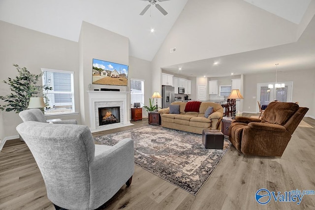 living room featuring ceiling fan with notable chandelier, a high end fireplace, high vaulted ceiling, and light hardwood / wood-style flooring