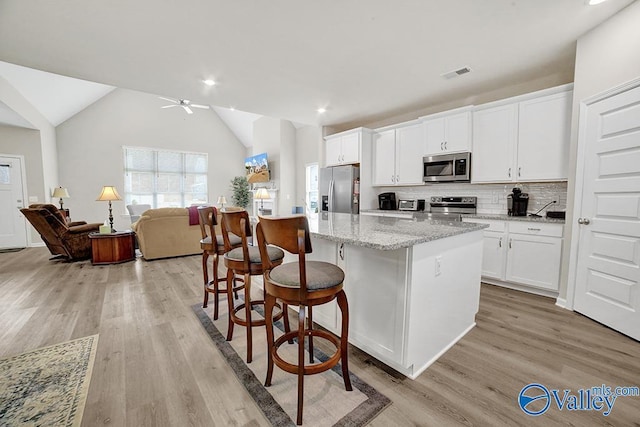 kitchen with a breakfast bar area, appliances with stainless steel finishes, white cabinetry, light stone counters, and an island with sink