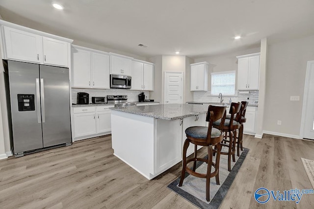 kitchen featuring a kitchen island, appliances with stainless steel finishes, a breakfast bar, white cabinets, and light stone counters