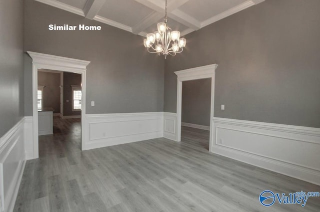 unfurnished dining area with a notable chandelier, coffered ceiling, beam ceiling, and wood finished floors