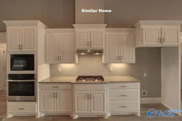 kitchen with white cabinets, appliances with stainless steel finishes, light stone countertops, and under cabinet range hood