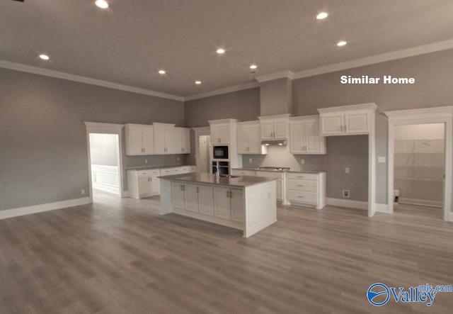 kitchen with dark countertops, a kitchen island with sink, black microwave, and white cabinets