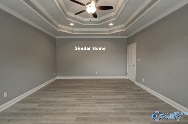 empty room featuring baseboards, ceiling fan, ornamental molding, wood finished floors, and a tray ceiling