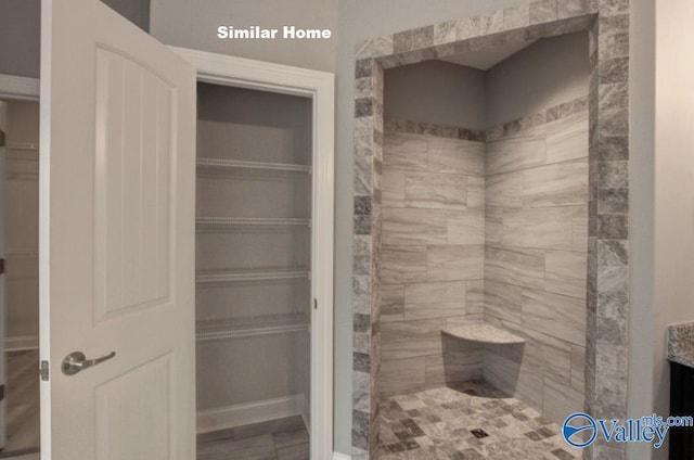 bathroom featuring a spacious closet, a tile shower, and vanity