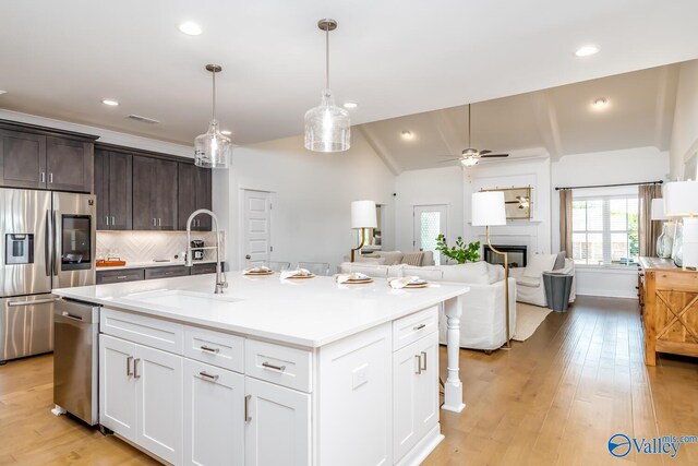 kitchen with light wood-type flooring, lofted ceiling, a center island with sink, and stainless steel appliances