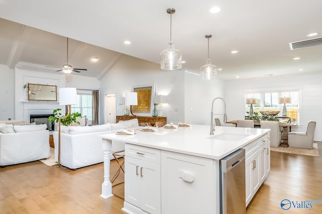 kitchen with light hardwood / wood-style flooring, a kitchen island with sink, stainless steel dishwasher, vaulted ceiling, and sink