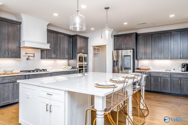 kitchen with decorative backsplash, appliances with stainless steel finishes, light wood-type flooring, and a center island with sink