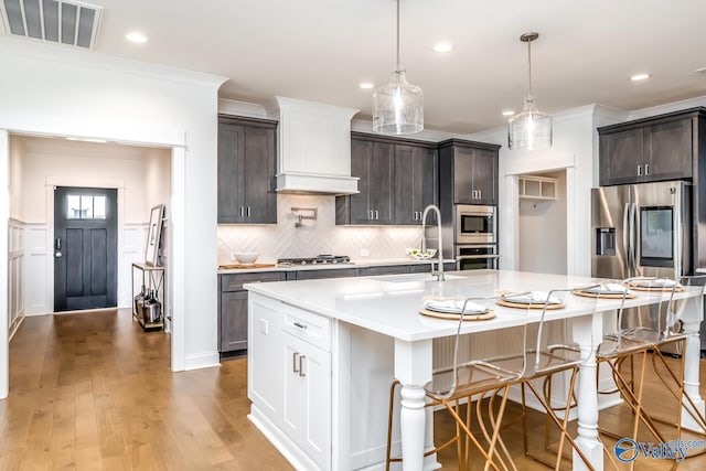 kitchen with backsplash, dark brown cabinetry, light wood-type flooring, and an island with sink