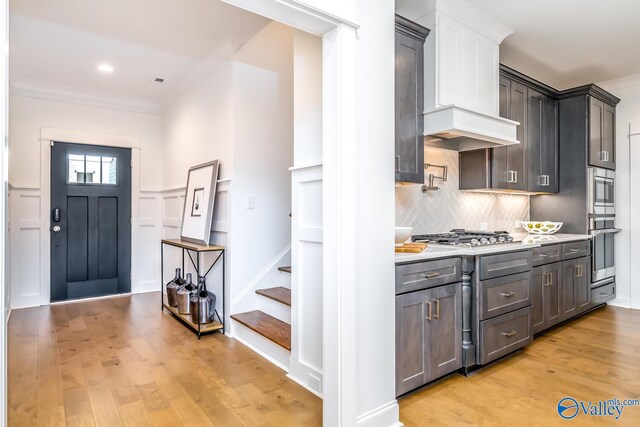 kitchen featuring crown molding, light hardwood / wood-style flooring, backsplash, premium range hood, and stainless steel appliances