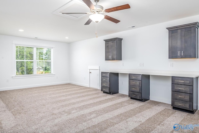 unfurnished office featuring light carpet, built in desk, and ceiling fan